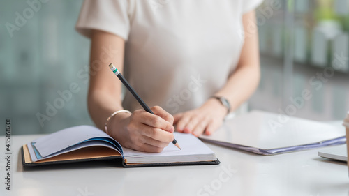 Image of a woman holding a pencil taking notes on the blank paper in the office.