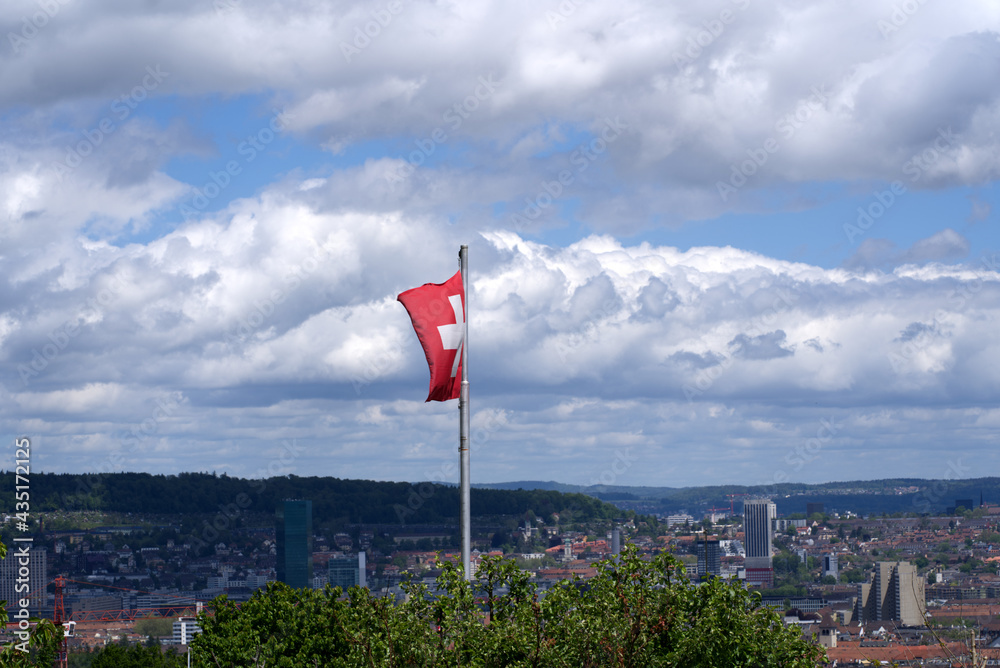 Swiss flag blowing in the wind with cityscape of Zurich in the background at springtime. Photo taken May 22nd, 2021, Zurich, Switzerland.