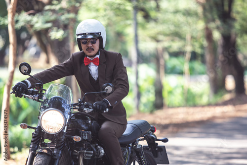 Rider riding modern classic motorcycle with suit look like gentleman for men campaign. Rider happy in freedom lifestyle travel by motorbike. photo