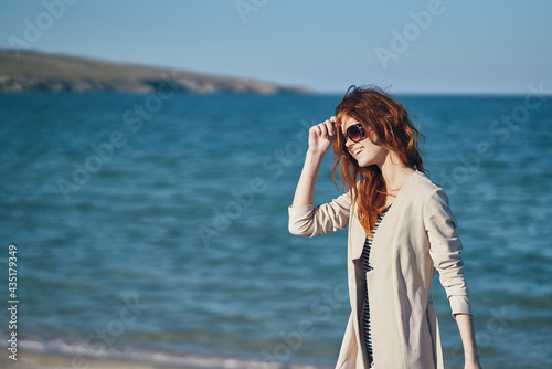 red-haired traveler in a coat and a t-shirt on the beach near the sea summer vacation