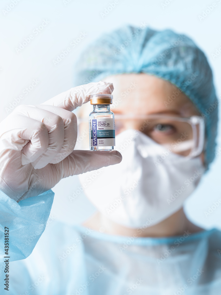 NO LOGOS OR TRADEMARKS!  SELF MADE LABELS! Close up view of doctor’s hand with an ampule of covid vaccine on blue back