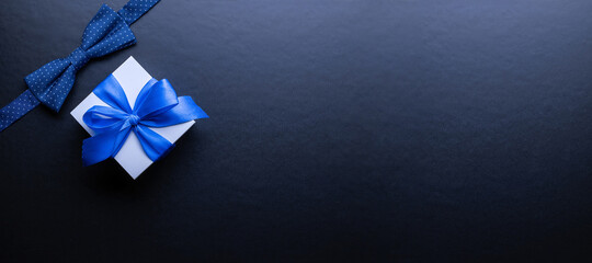 Gift father day. Blue bowtie or tie, white box with bow ribbon on dark background. Happy loving family and Fathers Day concept.