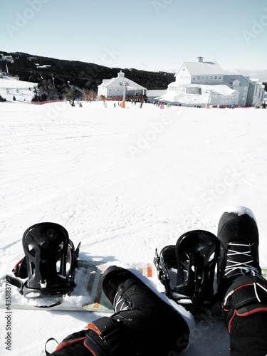 a young man taking a break from snowboarding with resort building view