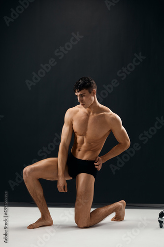 athletic man with a pumped-up body is kneeling in dark Studio panties