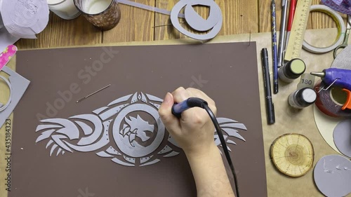 Women's hands make holes with soldering iron in eva foam ornament. Cosplayer workshop. Belt with image of dragon to Viking costume.