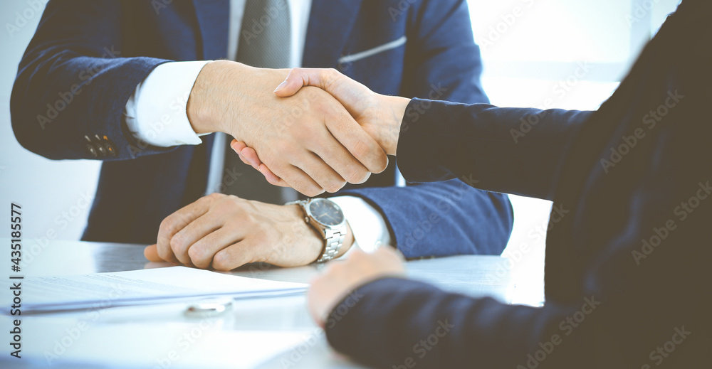 Businesspeople or lawyers shaking hands finishing up a meeting in blue toned office , close-up. Success at negotiation and handshake concepts