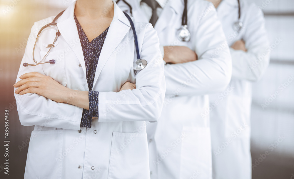 Doctors standing as a team with arms crossed in sunny clinic. Medical help, insurance and medicine concept Doctors standing as a team with arms crossed in sunny clinic. Medical help, insurance and medicine concept