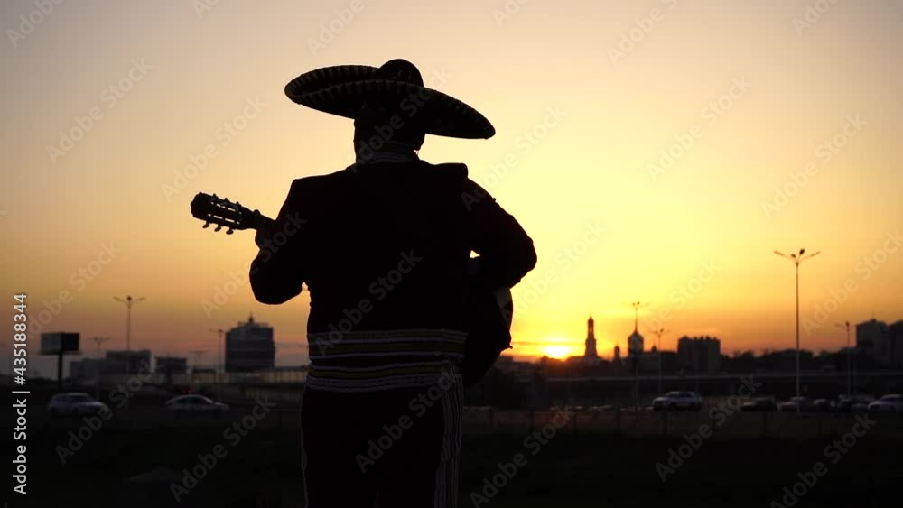 Silhouette of a mexican musician mariachi with a guitar on a background of city panorama. Slow motion