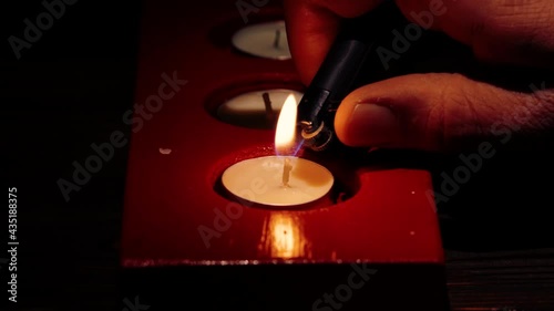Close-up macro footage of the hand that lights tea light candles in red candle holder in the darkness.