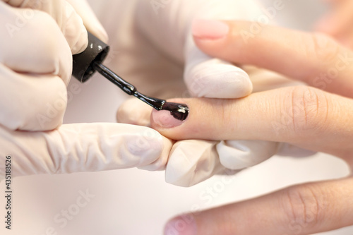 Manicure and nail coating of a young girl with black gel polish. Space for the text. The concept of professional nail care. Close-up.