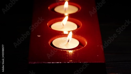 Close-up macro footage of the tea light candles light in red candle holder in the darkness.
