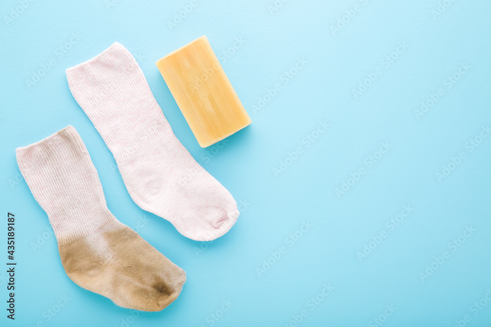 Baby socks and household soap on light blue table background. Pastel color. Detergent for clothes washing. Compare between dirty and clean socks. Problem and solution. Empty place for text. Top view. Baby socks and household soap on light blue table background. Pastel color. Detergent for clothes washing. Compare between dirty and clean socks. Problem and solution. Empty place for text. Top view.