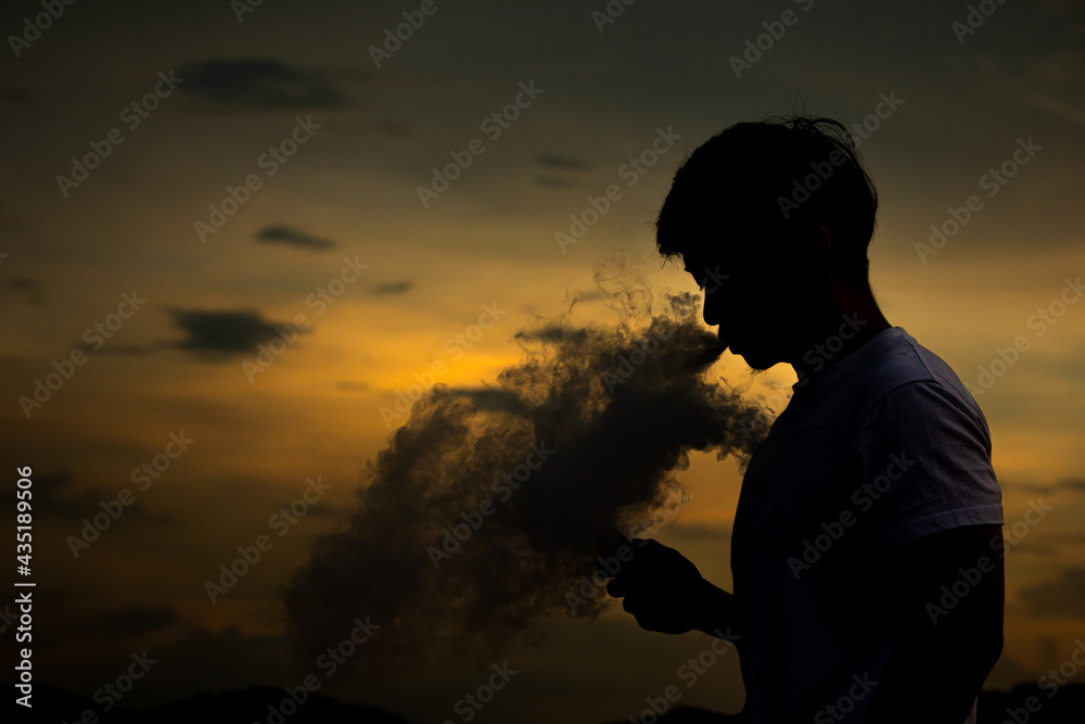 Obraz premium Man smoke electronic cigarette outdoor on beautiful sky background during sunset.