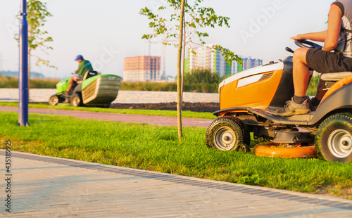 Workers drive lawn mowers tractors and mow the lawn in the park.