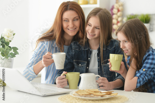 Beautiful young woman and girls sitting at table and using laptop and drinking tea