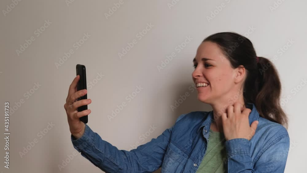 Young Caucasian woman on white background talks on video link using smartphone and looks at phone screen smiles rejoices and waves her hands. Important conversation over Internet online. 4K footage. Young Caucasian woman on white background talks on video link using smartphone and looks at phone screen smiles rejoices and waves her hands. Important conversation over Internet online. 4K footage.