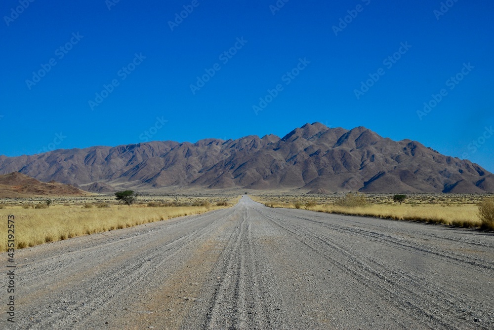 Gravel road leading towards mountains in the Namibian desert on a sunny day with blue sky and no clouds