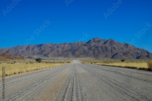 Gravel road leading towards mountains in the Namibian desert on a sunny day with blue sky and no clouds