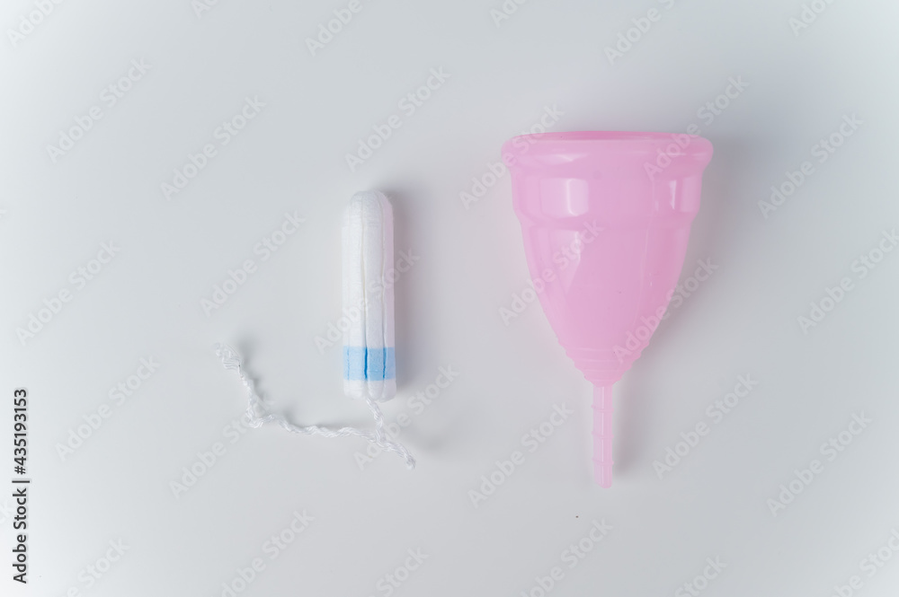 Pink menstrual cup and tampon on a white background. Various hygiene products during menstruation Pink menstrual cup and tampon on a white background. Various hygiene products during menstruation