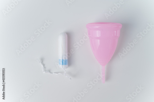 Pink menstrual cup and tampon on a white background. Various hygiene products during menstruation