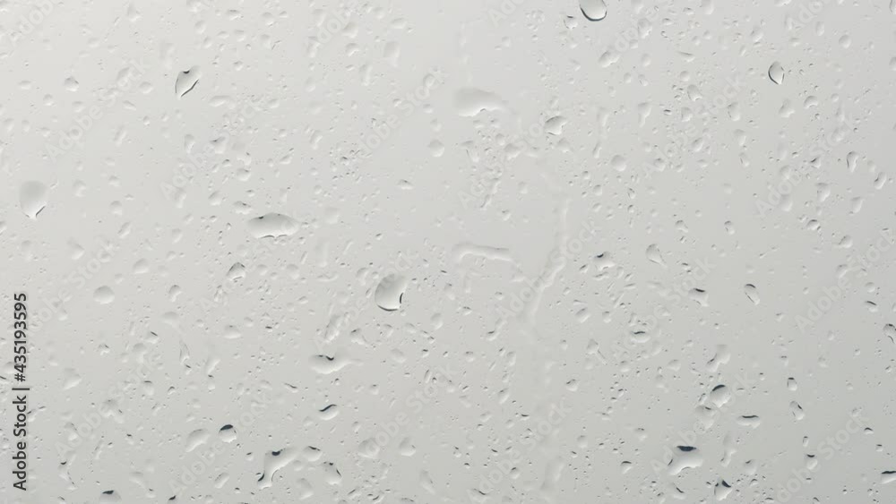 Drops flowing on glass. Rain is pouring down the window against a gray background. Drops flowing on glass. Rain is pouring down the window against a gray background.