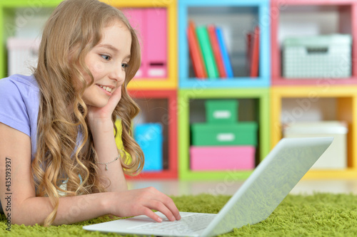 Cute girl using laptop while lying on green floor at home