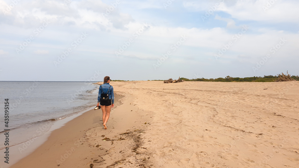 A woman with braided hair walking along the coastal line of a sandy beach by Baltic Sea on Sobieszewo island, Poland. The sea is gently waving. A bit of overcast. Solitude and serenity A woman with braided hair walking along the coastal line of a sandy beach by Baltic Sea on Sobieszewo island, Poland. The sea is gently waving. A bit of overcast. Solitude and serenity