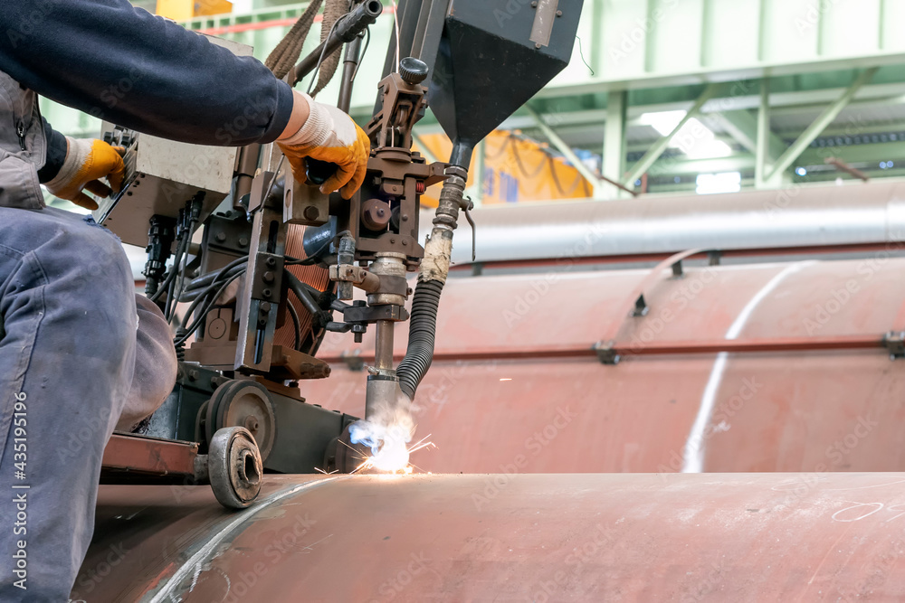 Fototapeta premium Welder operator is welding to pipe with submerged arc welding (SAW) method in the workshop. The process requires a continuously fed consumable solid or tubular (metal cored) electrode.