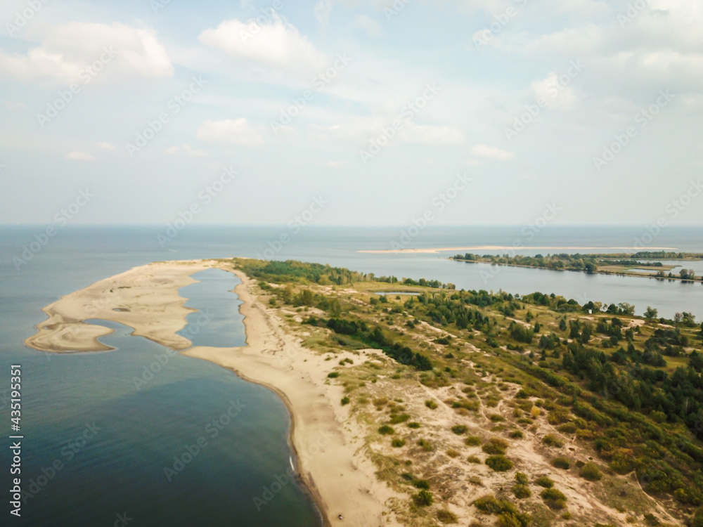 A areal shot of on Vistula Przekop - an area where Vistula river is merging with Baltic Sea on Sobieszewo island, Poland. The sea's side is sandy, the river's side is overgrown with trees.