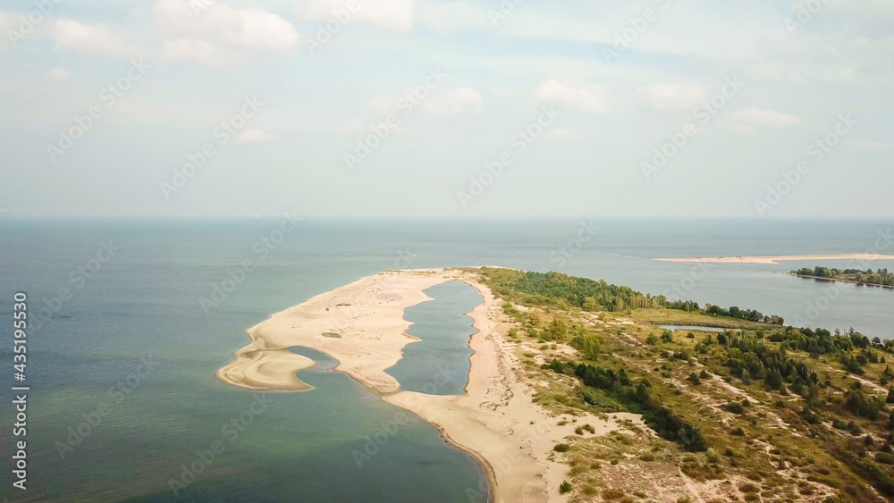 A areal shot of on Vistula Przekop - an area where Vistula river is merging with Baltic Sea on Sobieszewo island, Poland. The sea's side is sandy, the river's side is overgrown with trees.