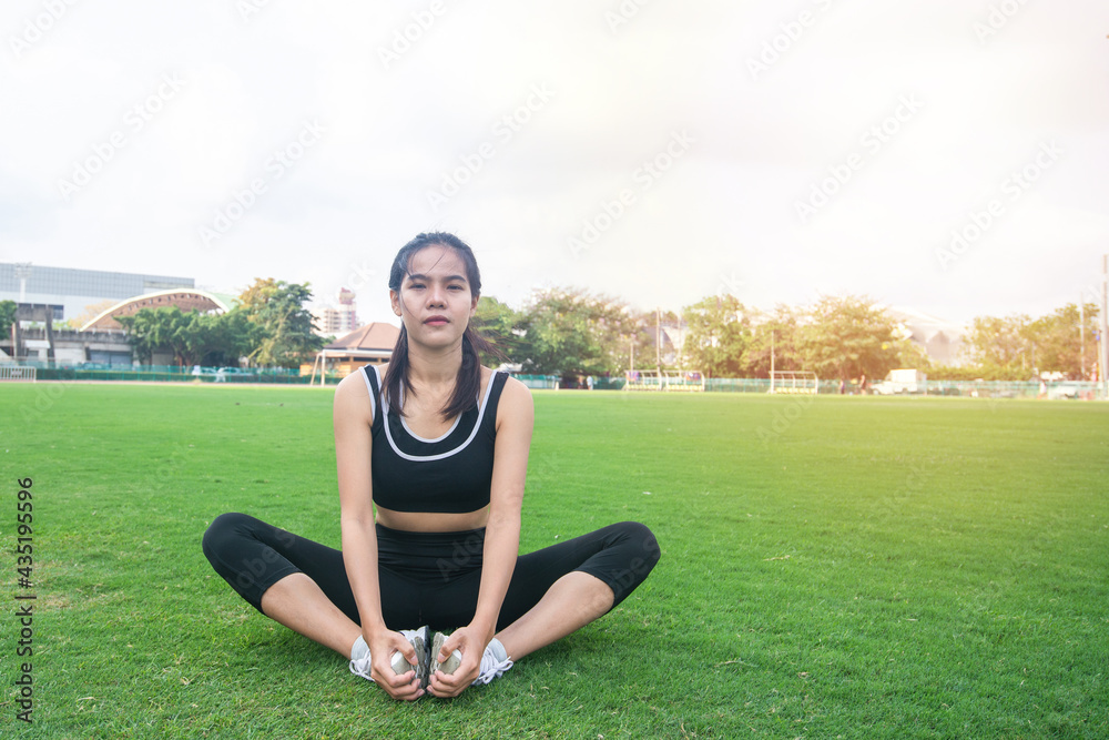 Fototapeta premium Portrait of beautiful young woman exercising on green grass. female fitness model stretching exercise or warming up before work out. exercise, Fitness, workout, sport, lifestyle concept.