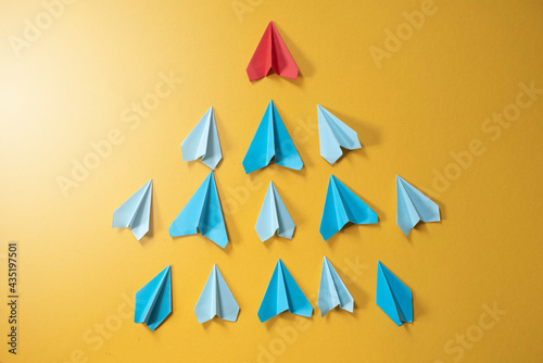 Fototapeta Naklejka Na Ścianę i Meble -  Blue paper aeroplane origami following rhe red one on yellow background