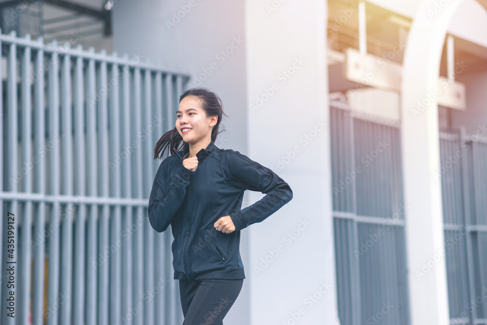 Medium shot Asian Beautiful Young woman black suit with happy running or jogging on blue running track in the day time. exercise, training, fitness, workout, sport, lifestyle and healthy concept. Medium shot Asian Beautiful Young woman black suit with happy running or jogging on blue running track in the day time. exercise, training, fitness, workout, sport, lifestyle and healthy concept.