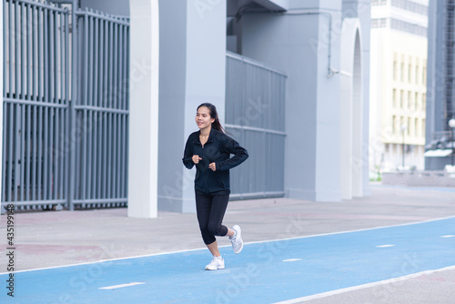 Asian Beautiful Young woman black suit with happy running or jogging on blue running track in the day time. exercise  training  fitness  workout  sport  lifestyle and healthy concept.