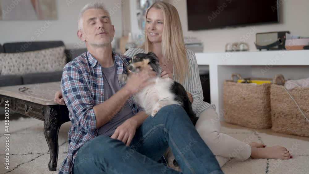 Happy couple with dog relaxing at home, sitting on carpet Happy couple with dog relaxing at home, sitting on carpet