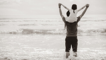 Little child girl riding on dads neck. Father and daughter standing on beach. Concept of Fathers day and Sepia color style
