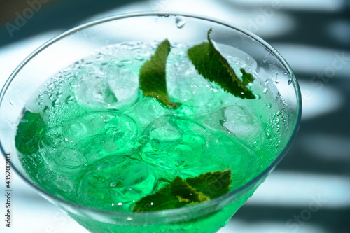 Glass of cocktail green fairy with lemon and mint leaves. Sweet refreshing mint liqueur, with ice and absinthe, rum, Ice cubes and Vodka