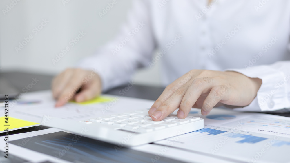 Fototapeta premium Young Asian businesswoman presses a calculator to calculate income tax and corporate income in a private office, Finance, Accounting, Tex, Statistical graphs of marketers investing in real estate.