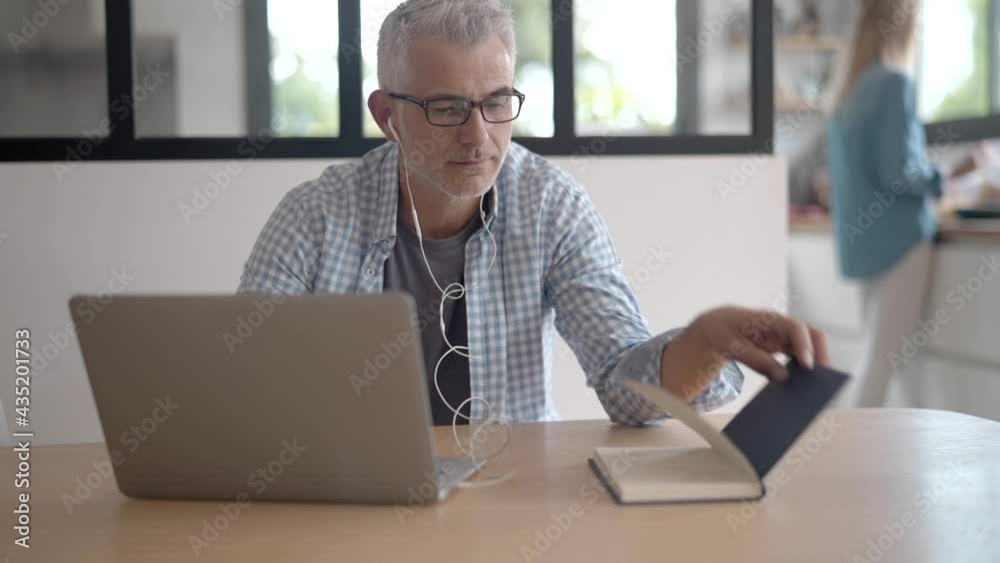 50-year-old man at home connected on laptop using earphones 50-year-old man at home connected on laptop using earphones