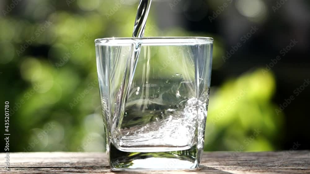 Close up pouring purified fresh clean drink water into glass from the bottle on old wooden table over sunlight nature background, feel refreshing in early morning. Healthy and Drinking Water Concept.
