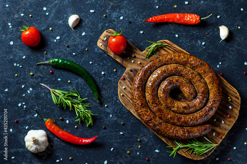 Snail sausage baked in an old oven is on a wooden board with pepper , garlic and rosemary. photo