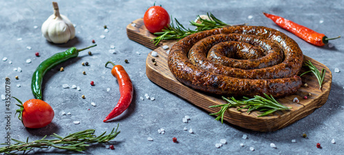 Snail sausage baked in an old oven is on a wooden board with pepper , garlic and rosemary.