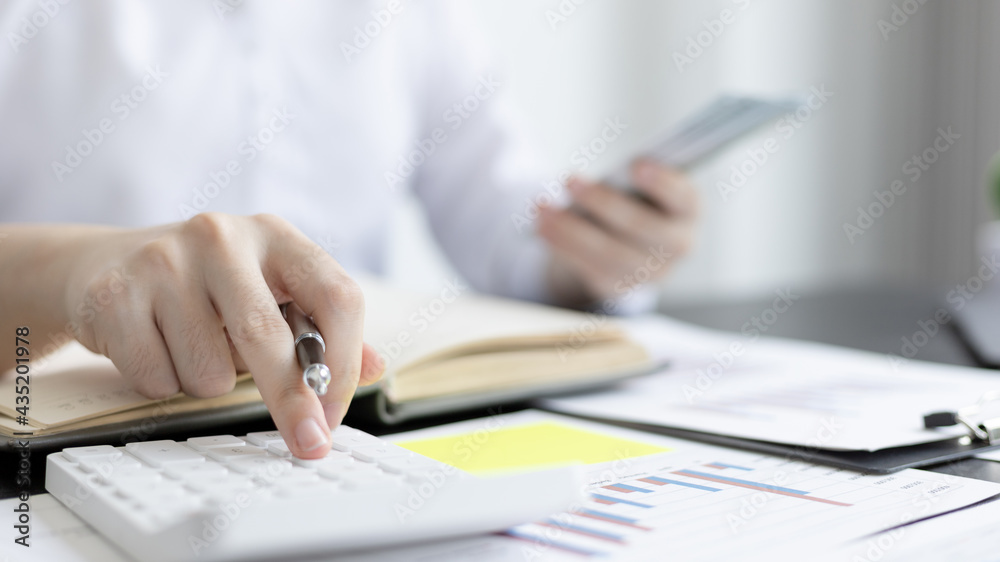 Business women press calculator to calculate company income and expenses, Calculating financial and tax information, Hand holding dollar bills, Financial savings and income tax calculation concept. Business women press calculator to calculate company income and expenses, Calculating financial and tax information, Hand holding dollar bills, Financial savings and income tax calculation concept.