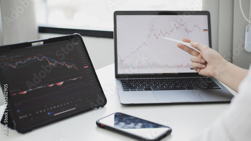 Investors sit and watch graphs of stock market data and watch the world market chart change, Investing in cryptocurrency in the stock market, Business people work on tablets and laptops. © Puwasit Inyavileart