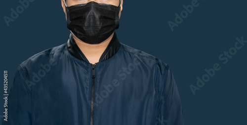 A young model in a dark blue long sleeve shirt, wearing a black mask against COVID-19 on a dark blue background.