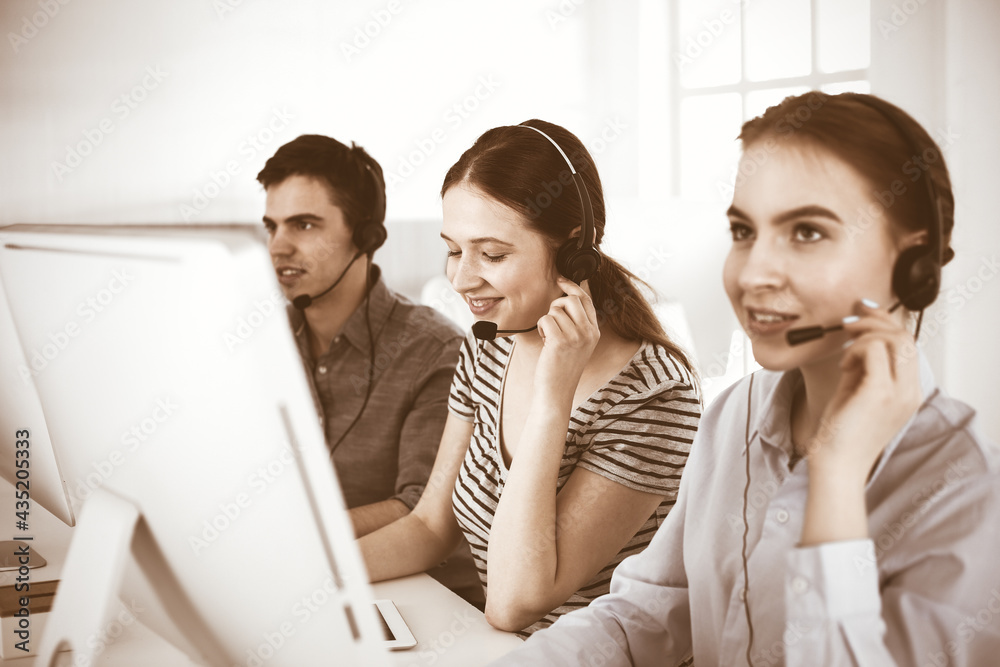 Casual dressed young woman using headset and computer while talking with customers online. Group of operators at work. Call center, business concept Casual dressed young woman using headset and computer while talking with customers online. Group of operators at work. Call center, business concept