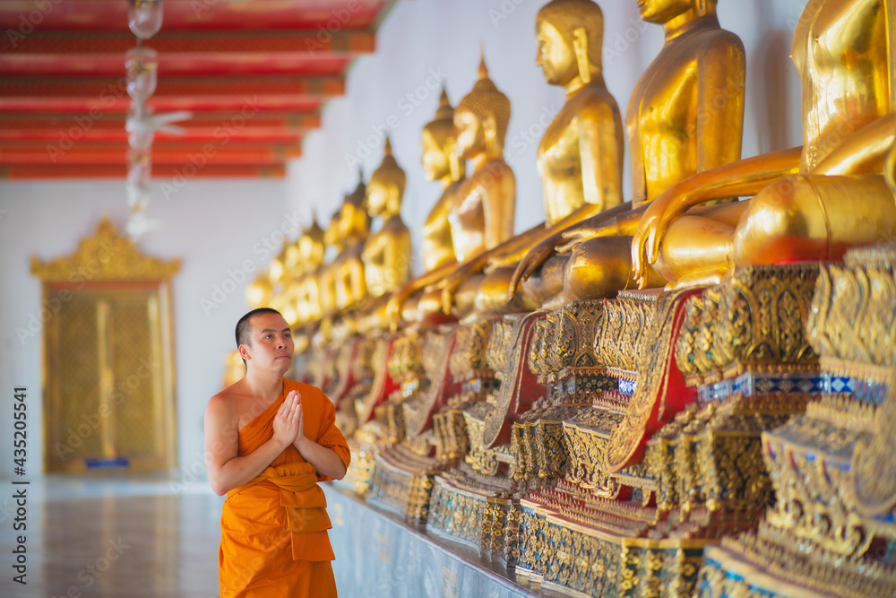 Fototapeta premium Monk walking down the hallway with buda statues around him