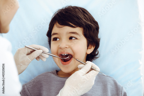 Cute arab boy sitting at dental chair with open mouth during oral checking up with doctor. Visiting dentist office. Stomatology concept