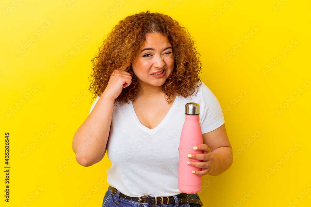 Young latin woman holding a thermos isolated on yellow background covering ears with hands. Young latin woman holding a thermos isolated on yellow background covering ears with hands.