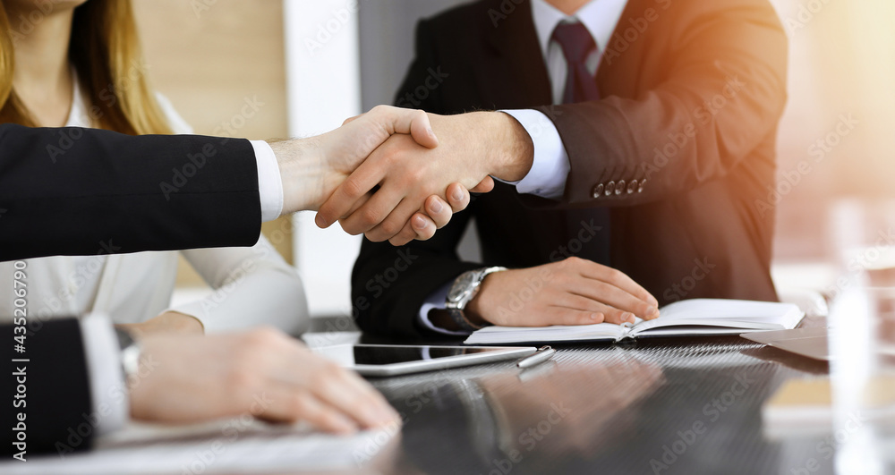 Businessman shaking hands with his colleague above the glass desk in sunny modern office, close-up. Unknown business people at meeting Businessman shaking hands with his colleague above the glass desk in sunny modern office, close-up. Unknown business people at meeting